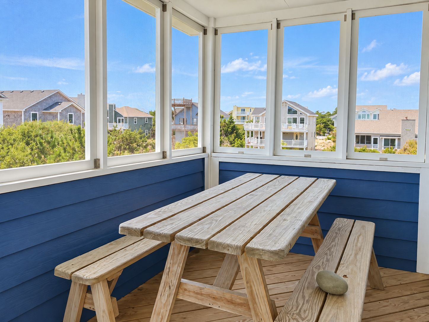 A covered patio with a wooden table and benches, large windows offering a view of residential buildings.