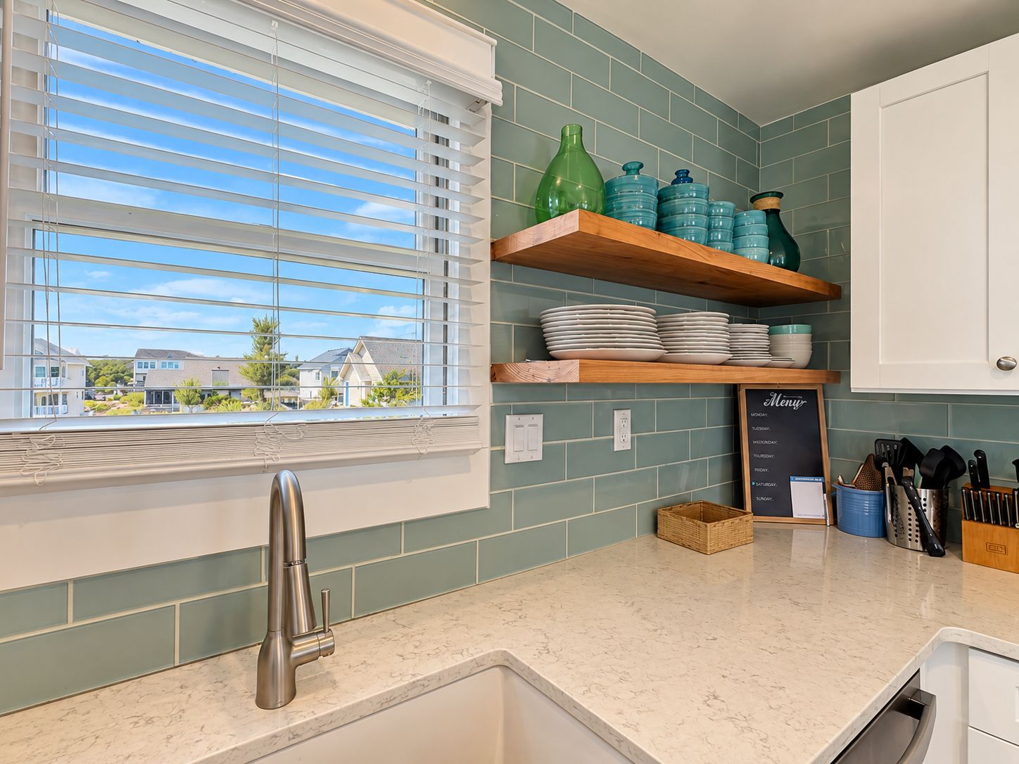 A kitchen with a window, a sink, and a shelf with kitchenware.