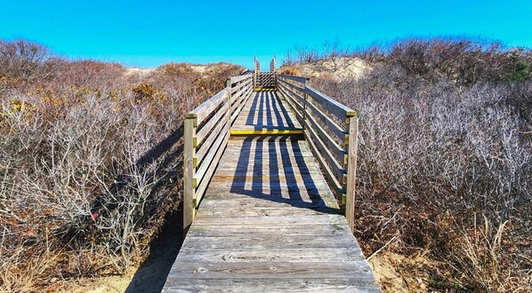 Une promenade en bois menant à une plage, entourée d’une végétation aride.