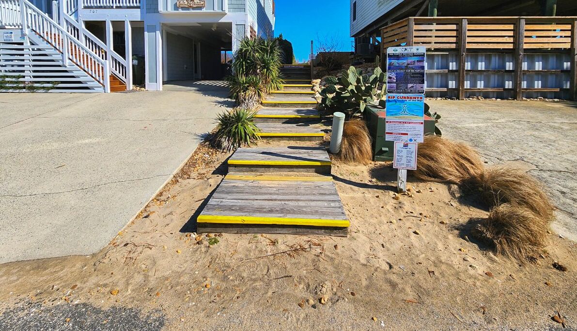 A pathway leading to a building with a staircase and a signboard.