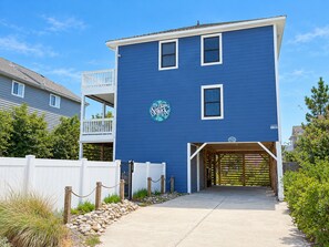 Un bâtiment à deux étages, avec une façade bleue, une clôture blanche et une entrée fermée par un portail.