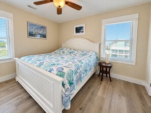 Ein Schlafzimmer mit einem Bett, einem Deckenventilator und zwei Fenstern mit Jalousien.