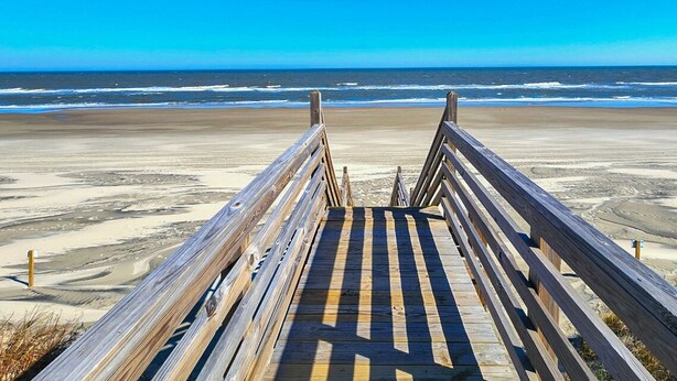 A wooden boardwalk leading to a beach with a clear view of the ocean.