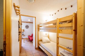 Una habitación con una cama litera, una puerta de madera, una mesita pequeña y una silla roja.