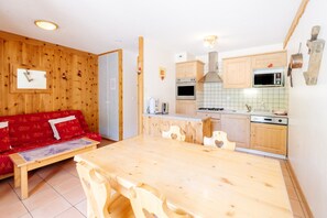 Un intérieur en bois comprenant une table à manger, des meubles de rangement en bois, un canapé rouge et un coin cuisine.