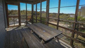 Una terraza de madera con una mesa de picnic y amplios ventanales que ofrecen vistas del paisaje circundante.