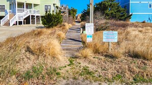 Un muelle de madera que lleva a una propiedad frente a la playa, con un cartel que indica el cobro por acceso a la playa.