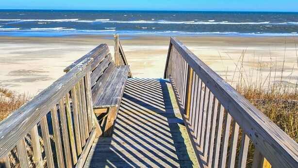 Pasarela de madera que conduce a una playa con vistas al océano.