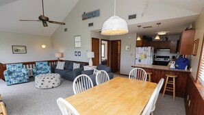 Una sala de estar acogedora con una mesa de comedor de madera, sillas blancas, un sofá y otomanas estampadas.