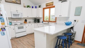 A kitchen with white cabinets, a white island with stools, a microwave, a stove, and a coffee maker. - Dunes Crest - Ocean and sound views in Duck, NC! 5 bed, 4.2 bath, pool, hot tub (Duck)