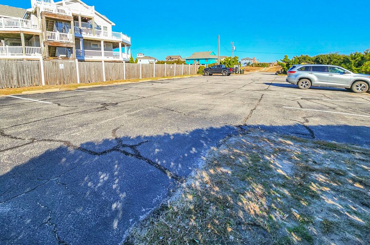 Ein Parkplatz mit beschädigter Asphaltdecke, einem Holzzaun und einem Gebäude mit Balkonen.