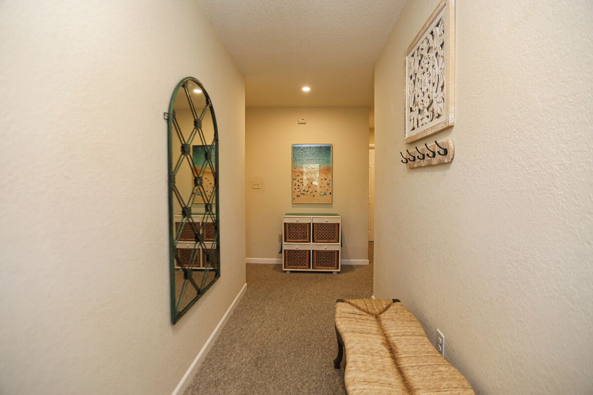 Un estrecho pasillo con un banco, un espejo decorativo, un mueble pequeño y una obra de arte enmarcada en la pared.