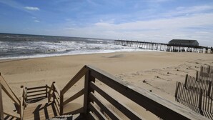 A wooden boardwalk leading to a beach with a pier in the background. - PELICAN'S LANDING - Beautiful semi-oceanfront townhouse with community pool, Great location! (Southern Shores)