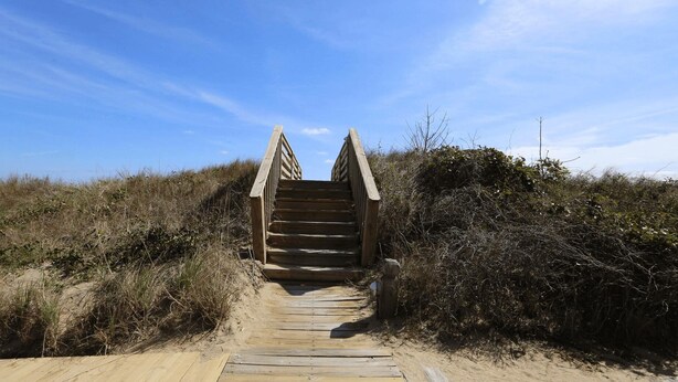 A wooden staircase leading up to a bridge over a sandy path, surrounded by dense shrubbery. - PELICAN'S LANDING - Beautiful semi-oceanfront townhouse with community pool, Great location! (Southern Shores)