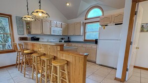 Una cocina con taburetes de madera, un refrigerador blanco y un microondas.