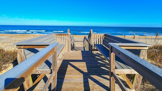 Un muelle de madera que conduce a una playa bajo un cielo azul despejado.