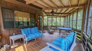 Un área de estar al aire libre techada, con suelo de madera, sofás a rayas azul y blanco y un ventilador de techo.