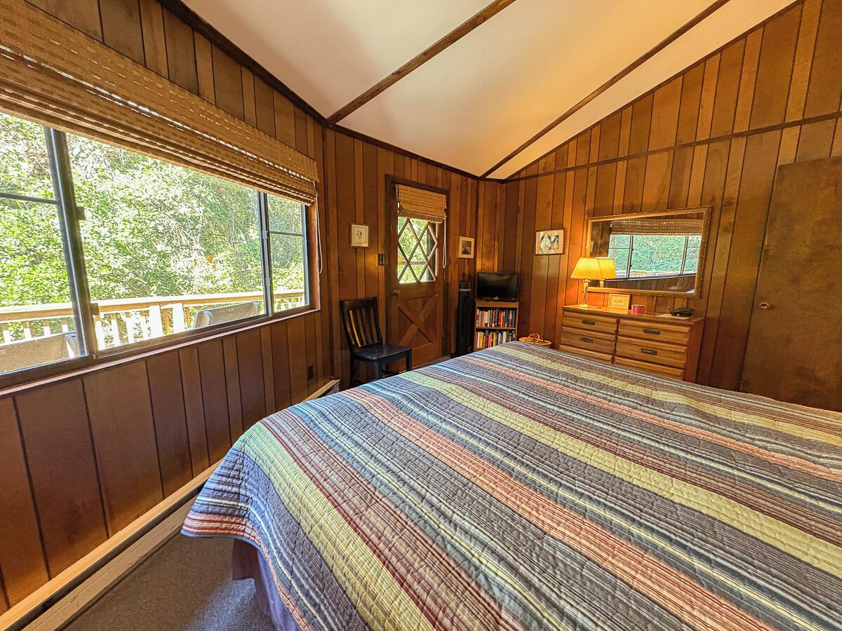 A bedroom with a large bed, wooden walls, a window, a chair, a dresser, and a television.