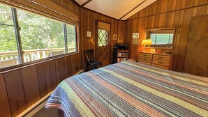 Un dormitorio con una cama grande, paredes de madera, una ventana, una silla, un aparador y un televisor.
