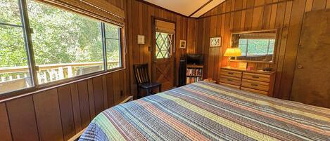 A bedroom with a large bed, wooden walls, a window, a chair, a dresser, and a television.
