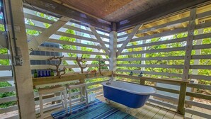 Une terrasse en bois avec une baignoire bleue, un banc blanc et un tapis à motifs.
