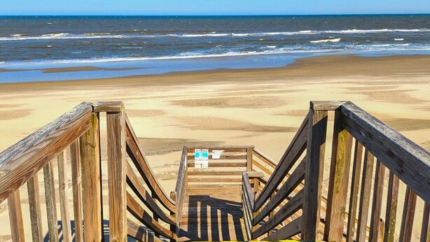 Une promenade en bois qui mène à une plage d’où l’on a une vue dégagée sur l’océan.