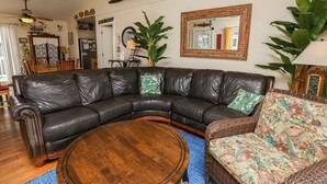Un salon avec un canapé d’angle en cuir, une table basse ronde et un fauteuil en osier.
