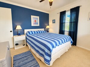 A bedroom with a bed, two bedside tables, a nightstand, a window with curtains, and a ceiling fan.