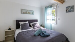 Ein Schlafzimmer mit Bett, Nachttisch, einem Fenster mit Vorhängen und einem an der Wand hängenden Kunstwerk.