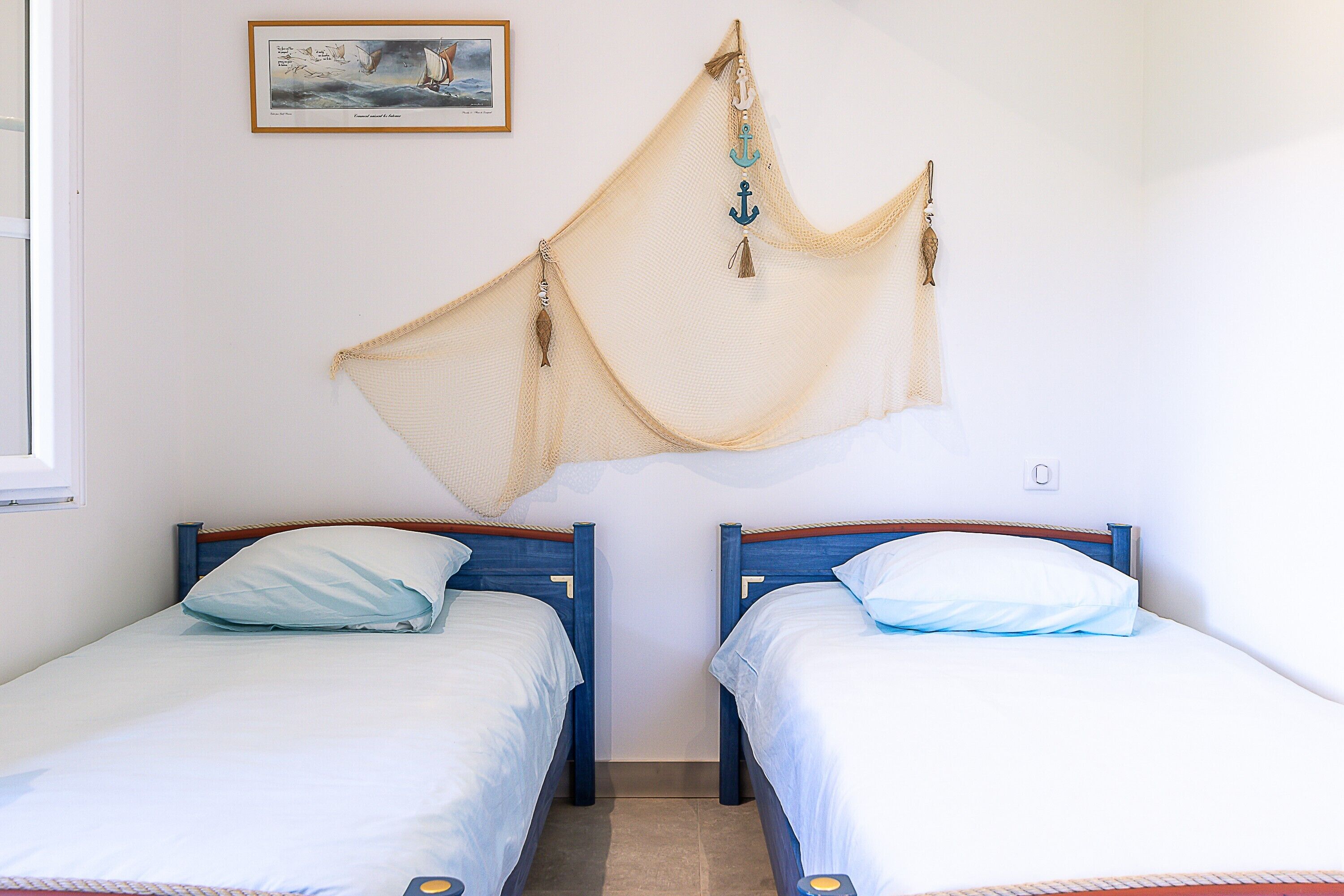 Dos camas individuales con cabeceros de madera, una mosquitera beige en la pared y un cuadro enmarcado sobre las camas.