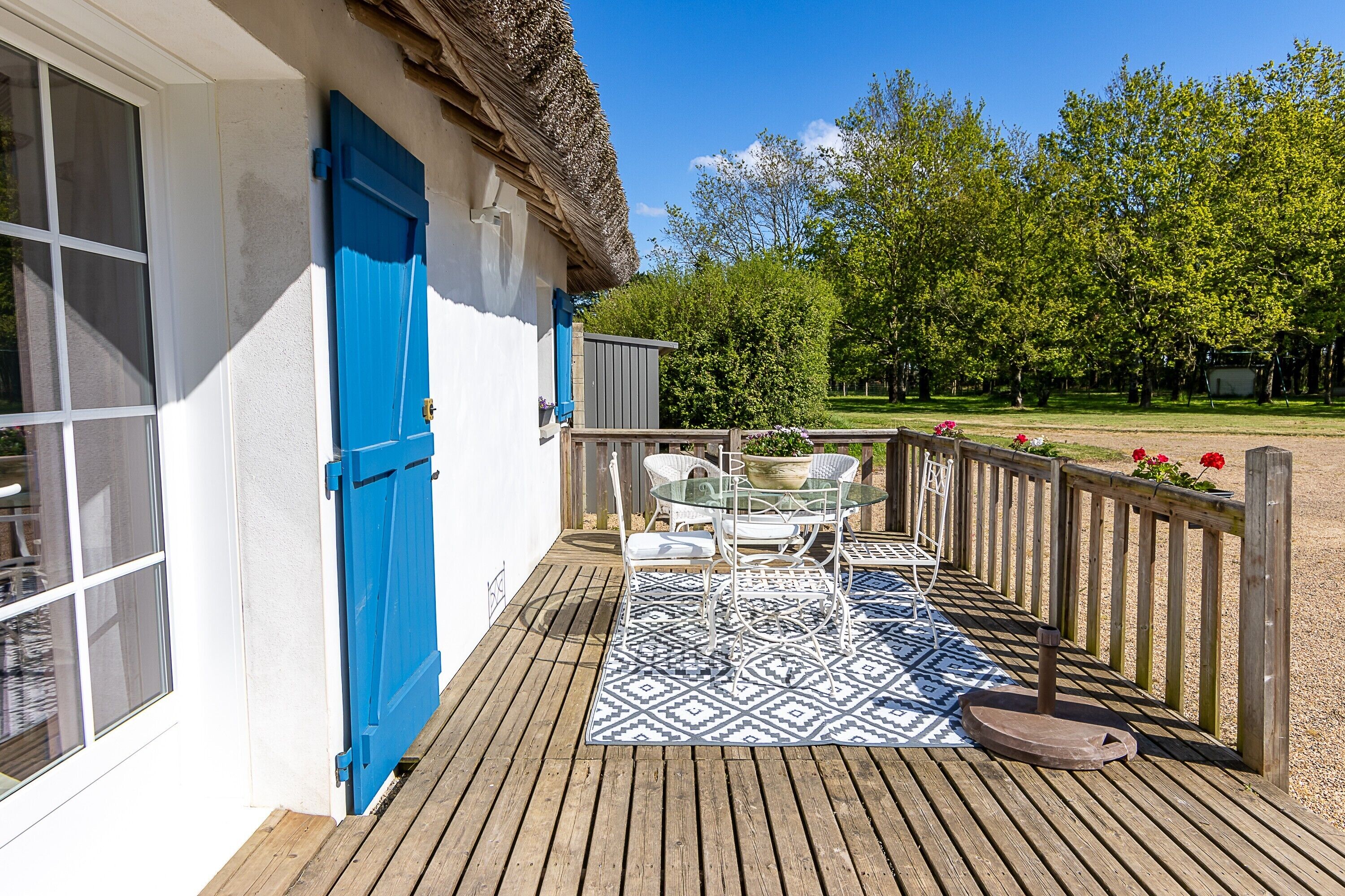 A wooden deck with a table and chairs, a blue door, and a white building.