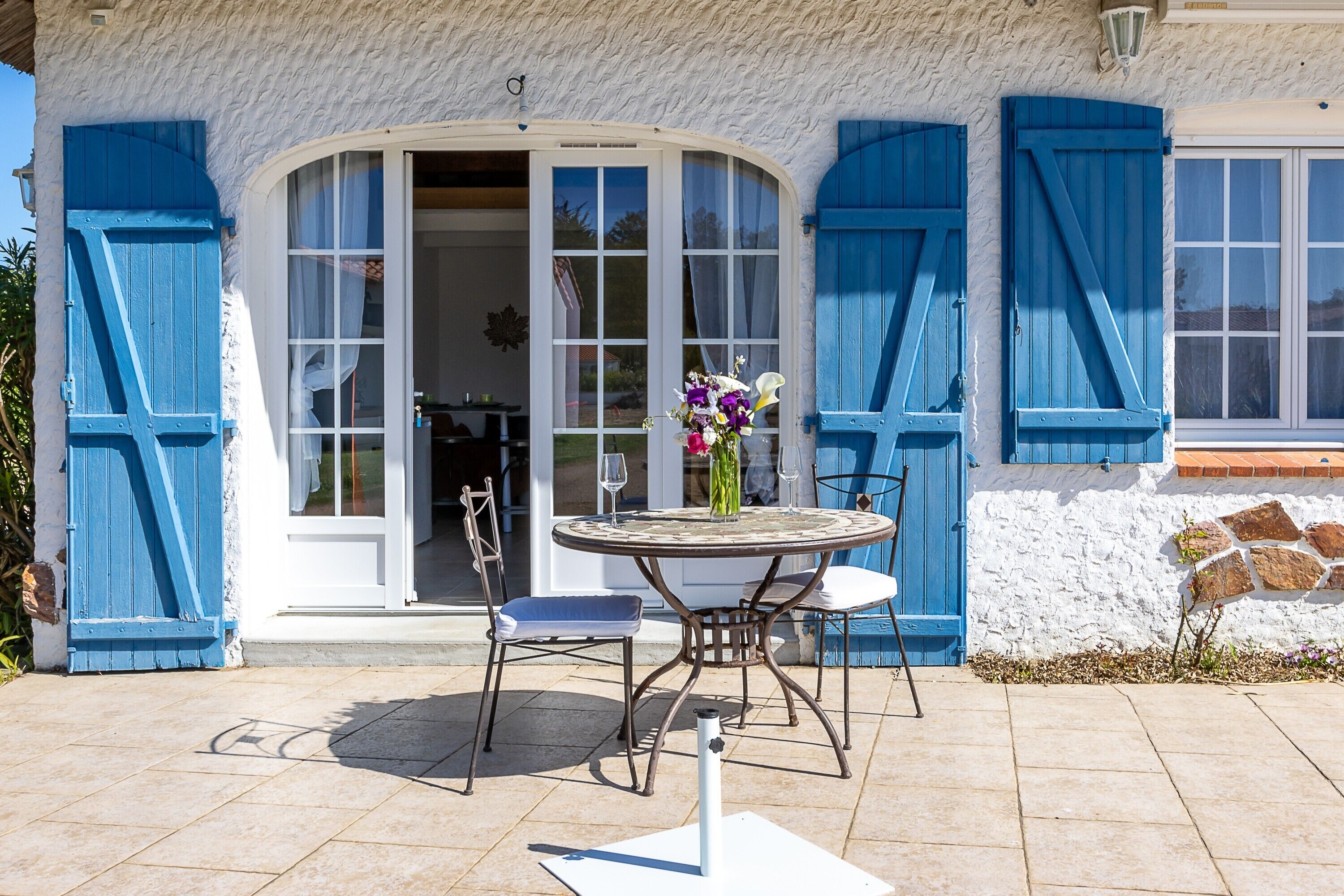 A house with a patio, a table with chairs, and a vase with flowers.