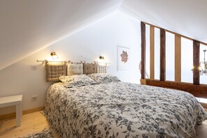 A bedroom with a bed, a bedside table, a wall-mounted light, and a wooden beam structure.