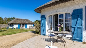 Une maison avec un toit de chaume, une terrasse avec une table et des chaises, et une porte bleue.