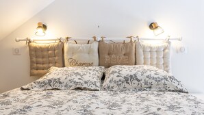 Un lit avec une literie à motifs floraux, une tête de lit à motifs capitonnés et deux lampes fixées au mur.