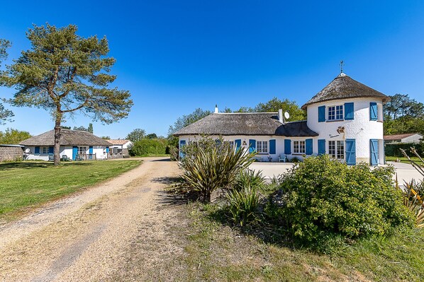 A two-story house with a thatched roof, a small tower, and a gravel driveway.