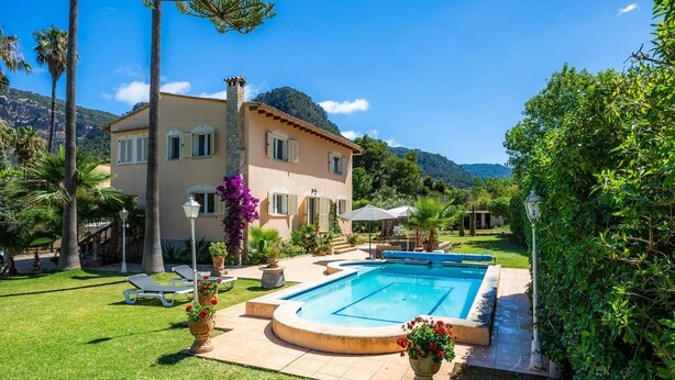 Une maison à deux étages avec une piscine, entourée de verdure et de palmiers.