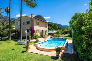 Uma casa de dois andares com piscina, cercada por vegetação e palmeiras.