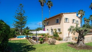 Une maison à deux étages avec une piscine, du mobilier d’extérieur et des palmiers.