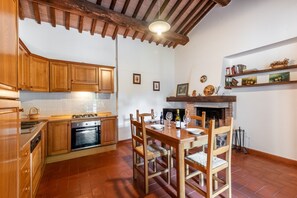 Une cuisine avec des meubles de rangement en bois, une table à manger avec des chaises, une cheminée et un mur recouvert de carreaux.