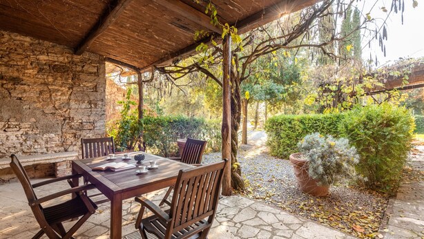 A covered patio with a stone table and wooden chairs, surrounded by greenery and a stone wall. - Apartment 'La Spiga' with Shared Pool, Shared Terrace and Wi-Fi (Rapolano Terme)