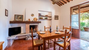 A dining area with a brick fireplace, wooden table, chairs, and a television. - Apartment 'La Spiga' with Shared Pool, Shared Terrace and Wi-Fi (Rapolano Terme)