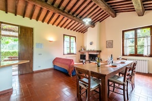 Un comedor amplio con una mesa y sillas de madera, chimenea y ventanas grandes.