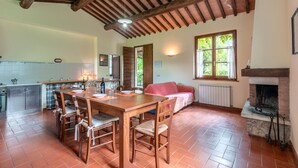 A rustic kitchen with a wooden table and chairs, a fireplace, and a dining area with a red sofa. - Apartment 'Il Covone' with Shared Pool, Shared Terrace and Wi-Fi (Rapolano Terme)