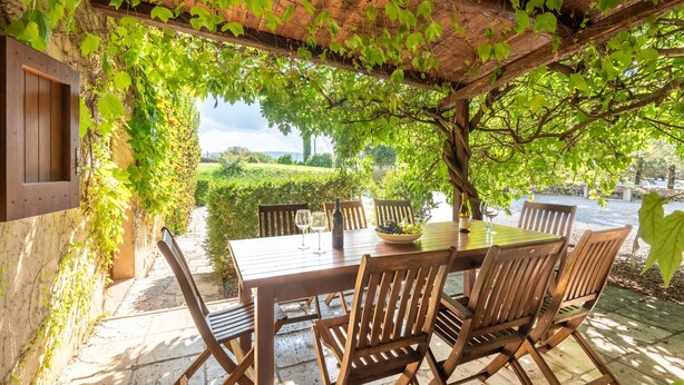 A wooden table set outdoors with chairs, a bottle, and glasses on it. - Apartment 'La Lollaia' with Shared Pool, Shared Terrace and Wi-Fi (Rapolano Terme)