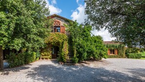 A stone building with a covered entrance, surrounded by lush greenery and a gravel driveway. - Apartment 'La Lollaia' with Shared Pool, Shared Terrace and Wi-Fi (Rapolano Terme)