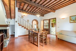 Un comedor con mesa y sillas de madera, chimenea y una escalera que sube a otra habitación.