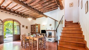A dining area with a wooden table and chairs, a fireplace, and a staircase. - Apartment 'La Lollaia' with Shared Pool, Shared Terrace and Wi-Fi (Rapolano Terme)