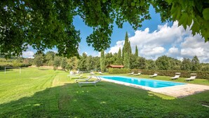 A swimming pool with lounge chairs, a well-maintained lawn, and a red-roofed building in the background. - Apartment 'La Lollaia' with Shared Pool, Shared Terrace and Wi-Fi (Rapolano Terme)