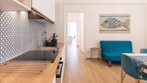 A modern kitchen with a patterned backsplash, a dining area with a blue sofa, and a fish artwork on the wall. - Apartment 'Capitan Trinchetto Risacca' with Balcony and Wi-Fi (Trapani)